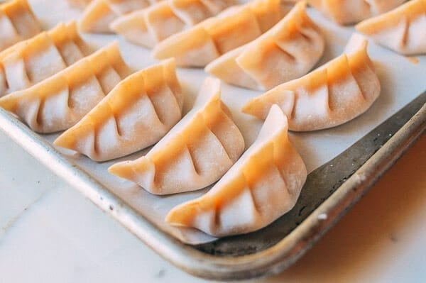 Heat pan over medium heat and add 2 tablespoons oil. Cook the onions and celery until translucent and transfer to a mixing bowl, along with the ground chicken, hot sauce, cheese, and salt and pepper to taste. Wet the edges of each dumpling wrapper with water, add about 2 teaspoons of filling in the center, and fold in half. You can also pleat them as shown in this post. Heat 2 tablespoons oil in a nonstick pan over medium high heat and add the potstickers. When they’re golden brown on the bottom, add 1/3 cup water to the pan. Cover and steam the potstickers until the water is evaporated. While that’s going, mix the blue cheese and the chopped green onion with the sour cream or yogurt. Season with salt and pepper to taste. Serve the dumplings along with the blue cheese sauce.