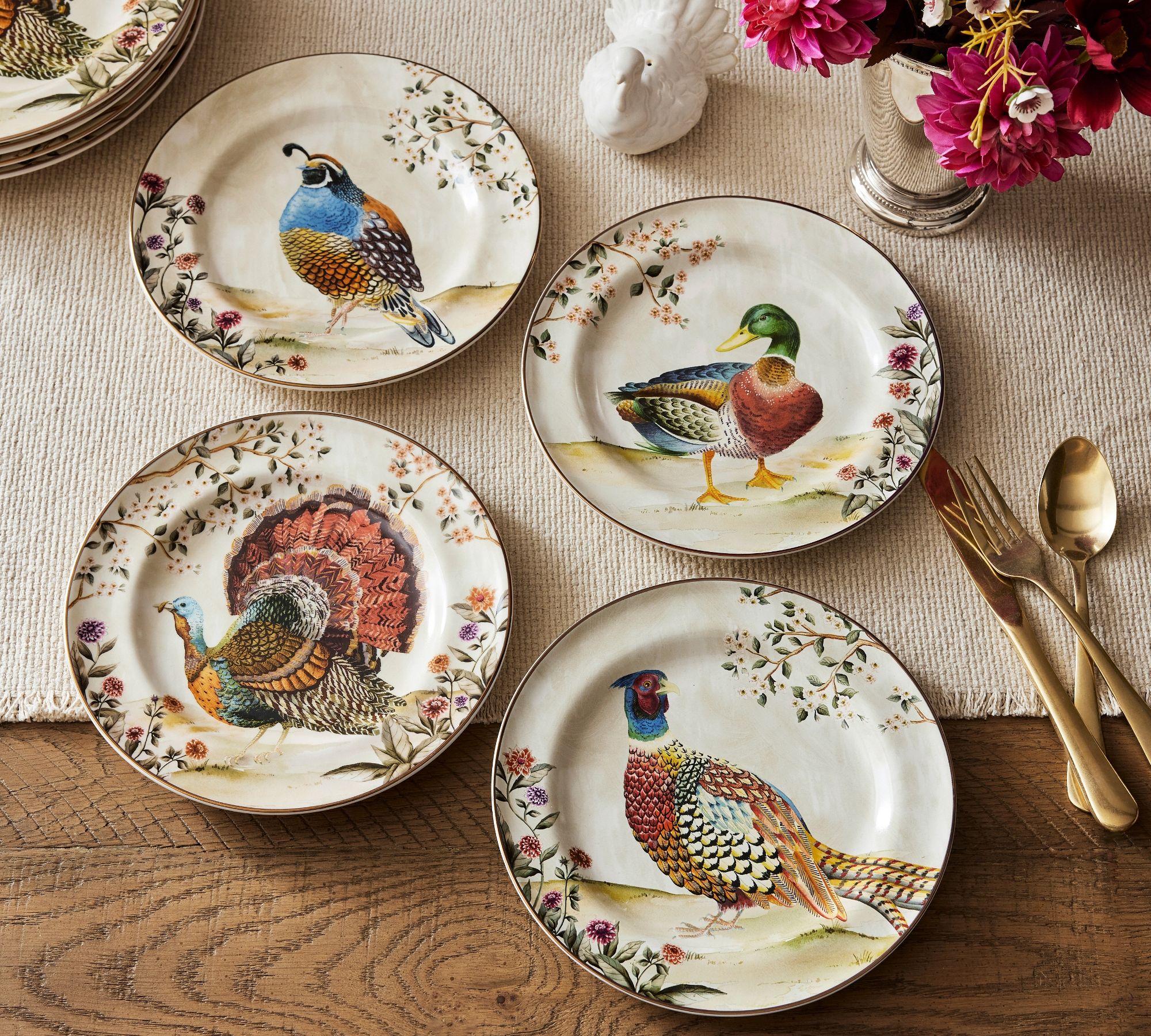 painted plates with quail, mallard, partridge, and turkey on each with a rustic tablesetting and gold flatware