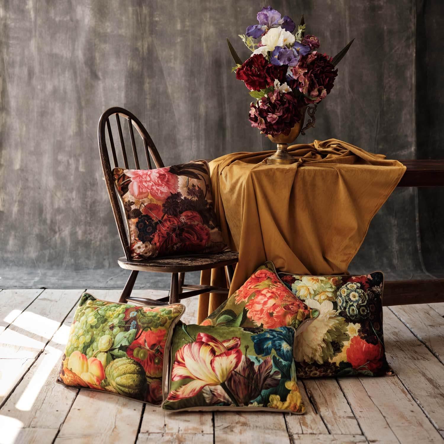 Art pillows with floral paintings arranged with a table, chair, and vase of flowers in a studio