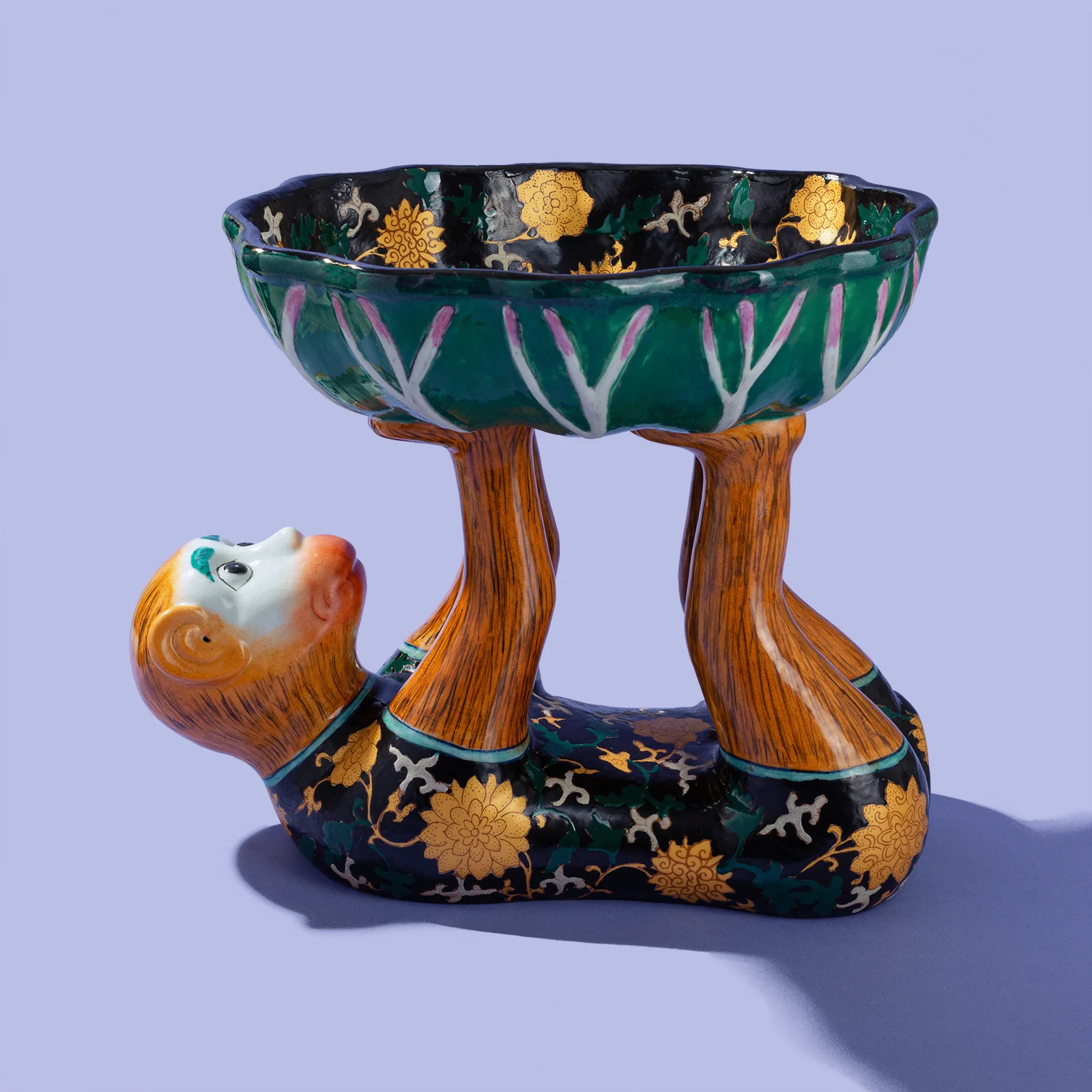 porcelain monkey holding up a lotus leaf bowl painted in black, gold, and teal
