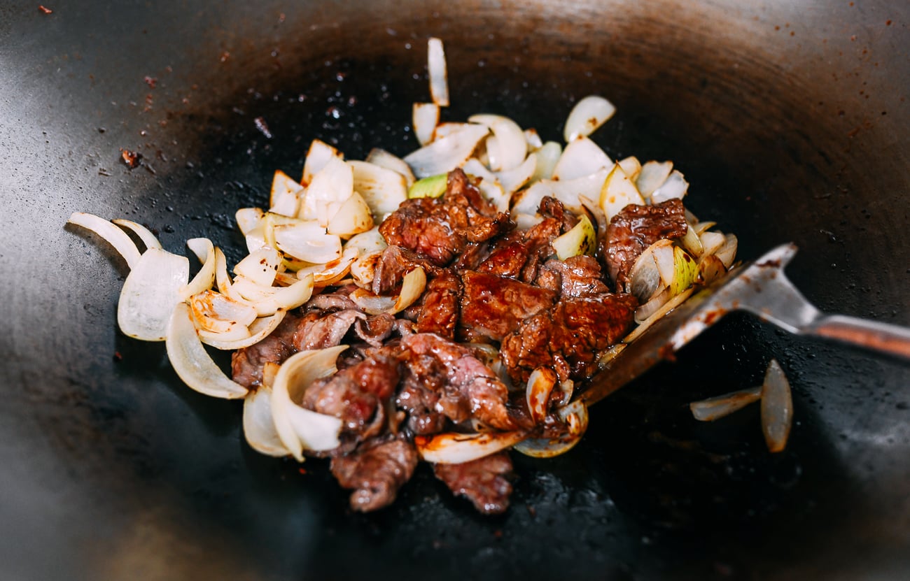 Stirring beef and onions into sauce in wok