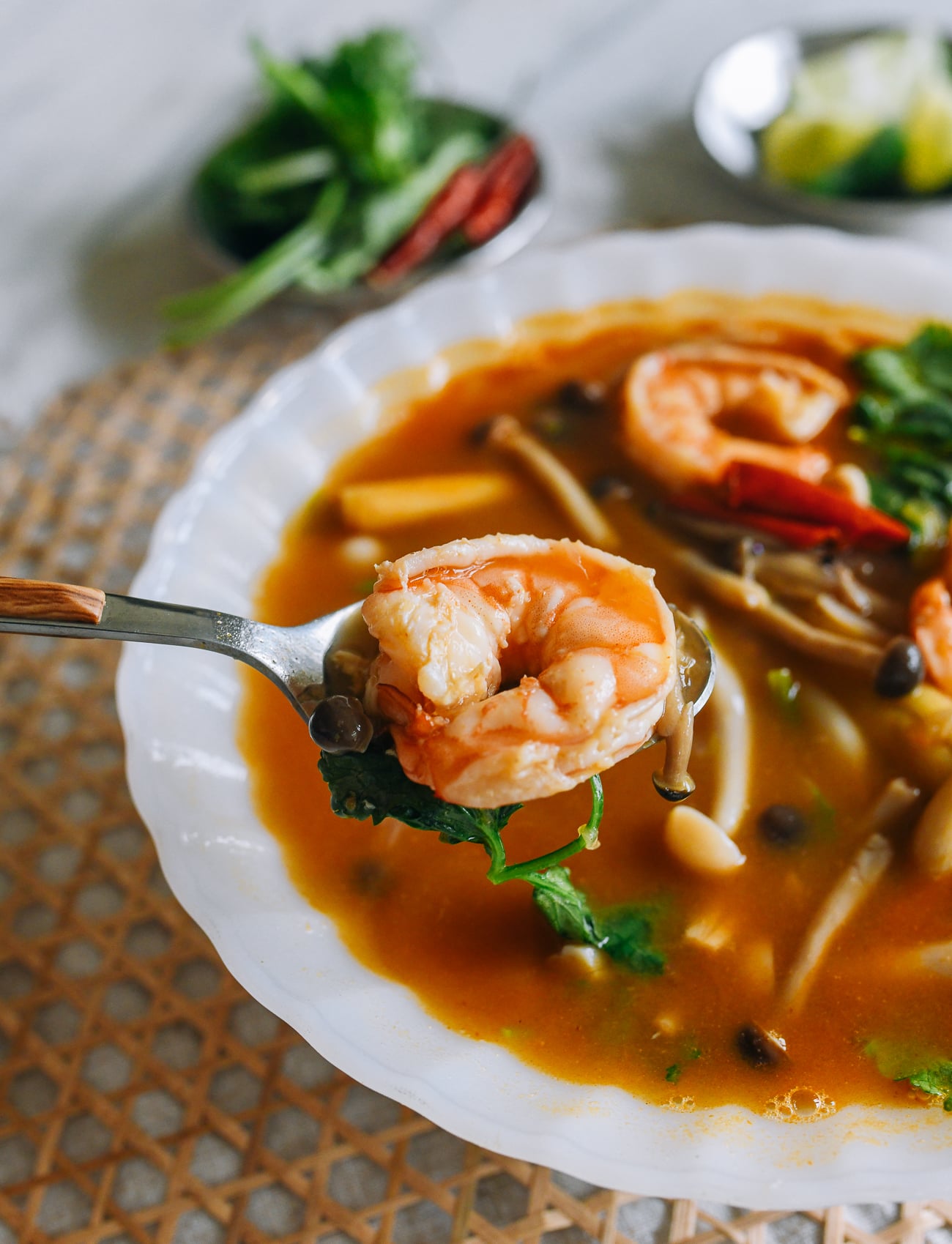 Picking up shrimp with a spoon from a bowl of tom yum soup
