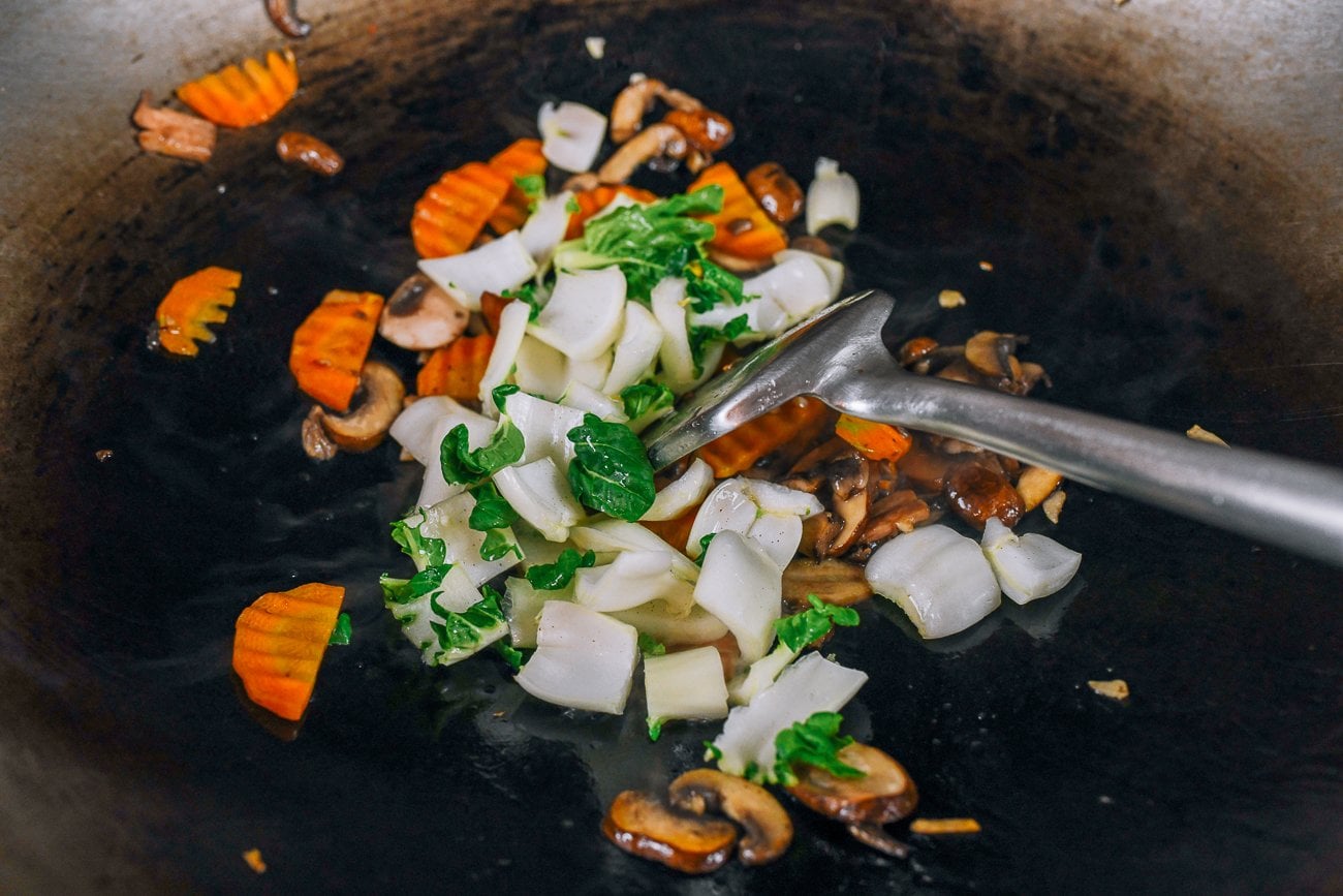 adding bok choy stems to vegetables in wok