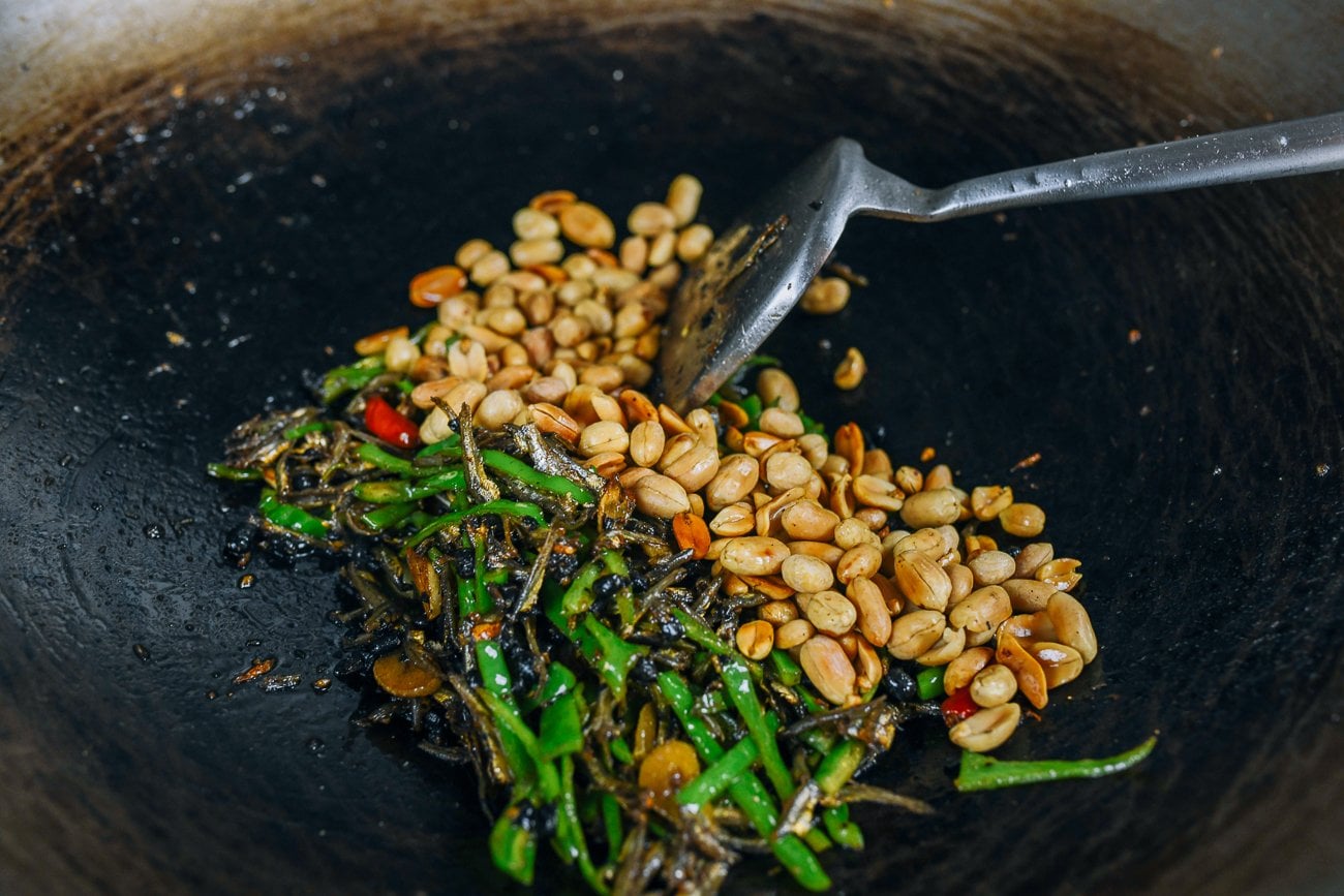 adding peanuts to anchovy stir-fry with peppers