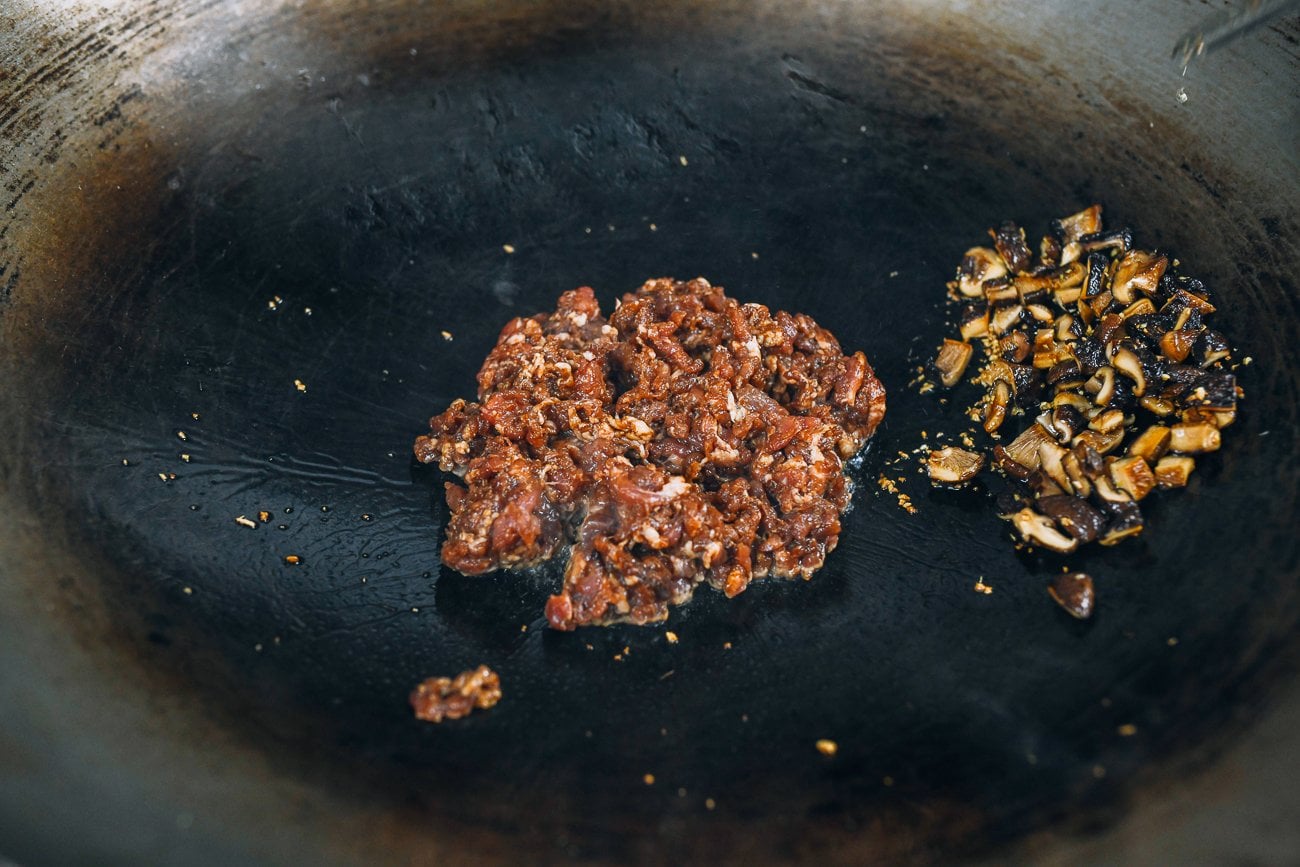 Wok with minced raw pork and shiitake mushrooms off to the side