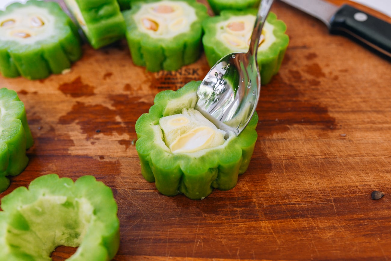 scooping seeds out of slice of bitter melon with spoon
