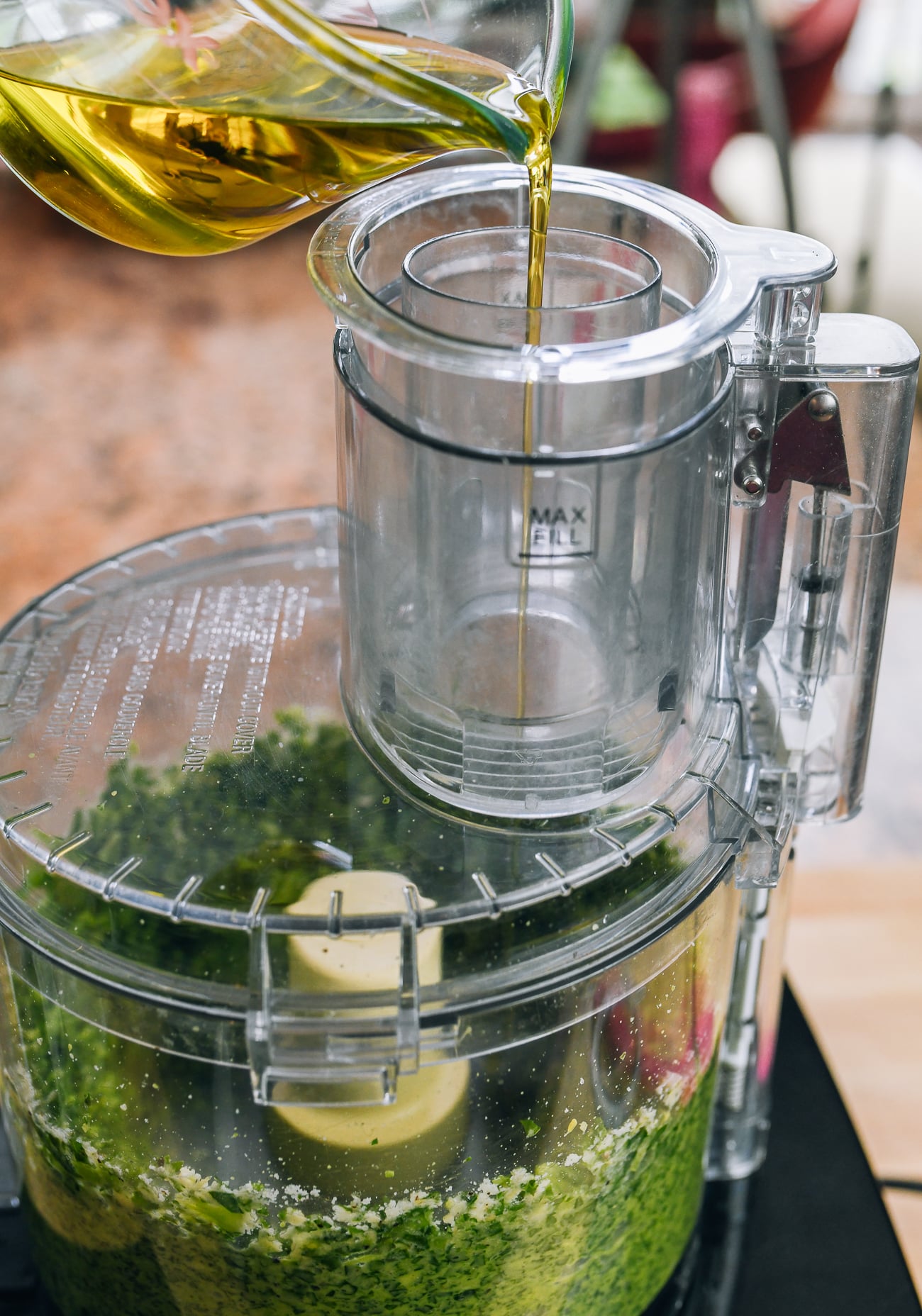 pouring extra virgin olive oil through feed tube to of food processor to make pesto
