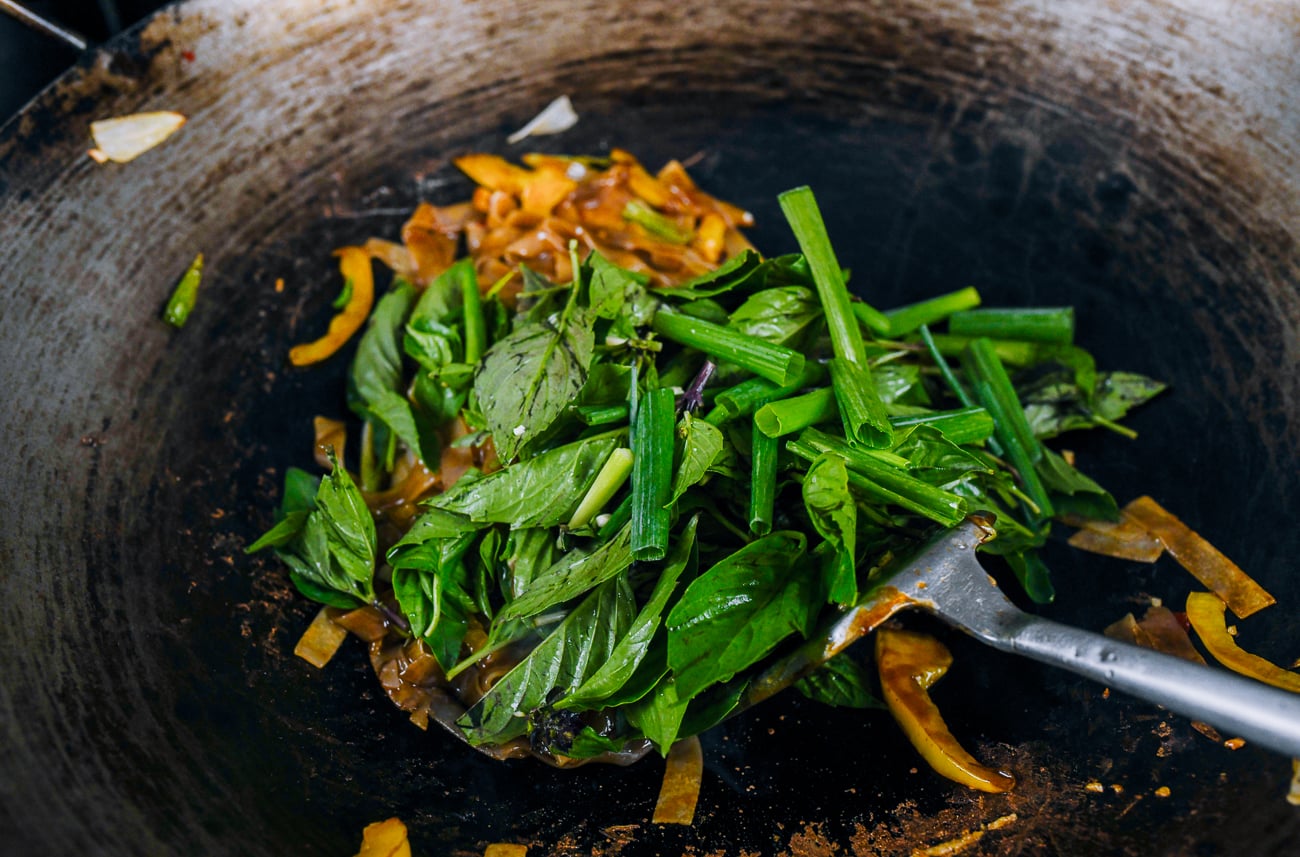 Thai basil and scallions added to noodles in wok