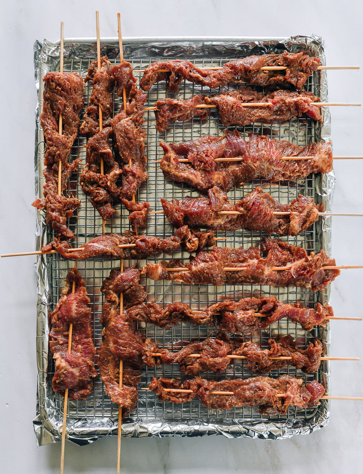 beef skewers laid out on wire rack on baking sheet