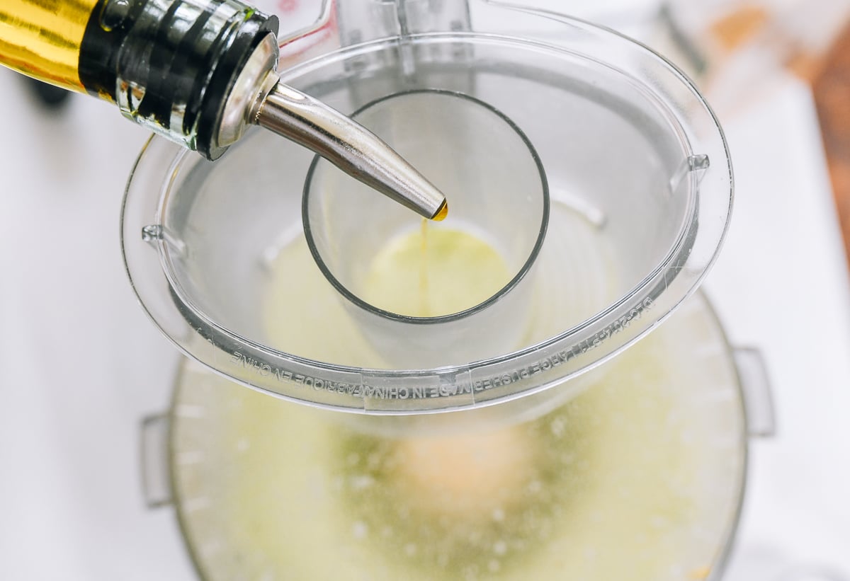 Pouring olive oil into running food processor 