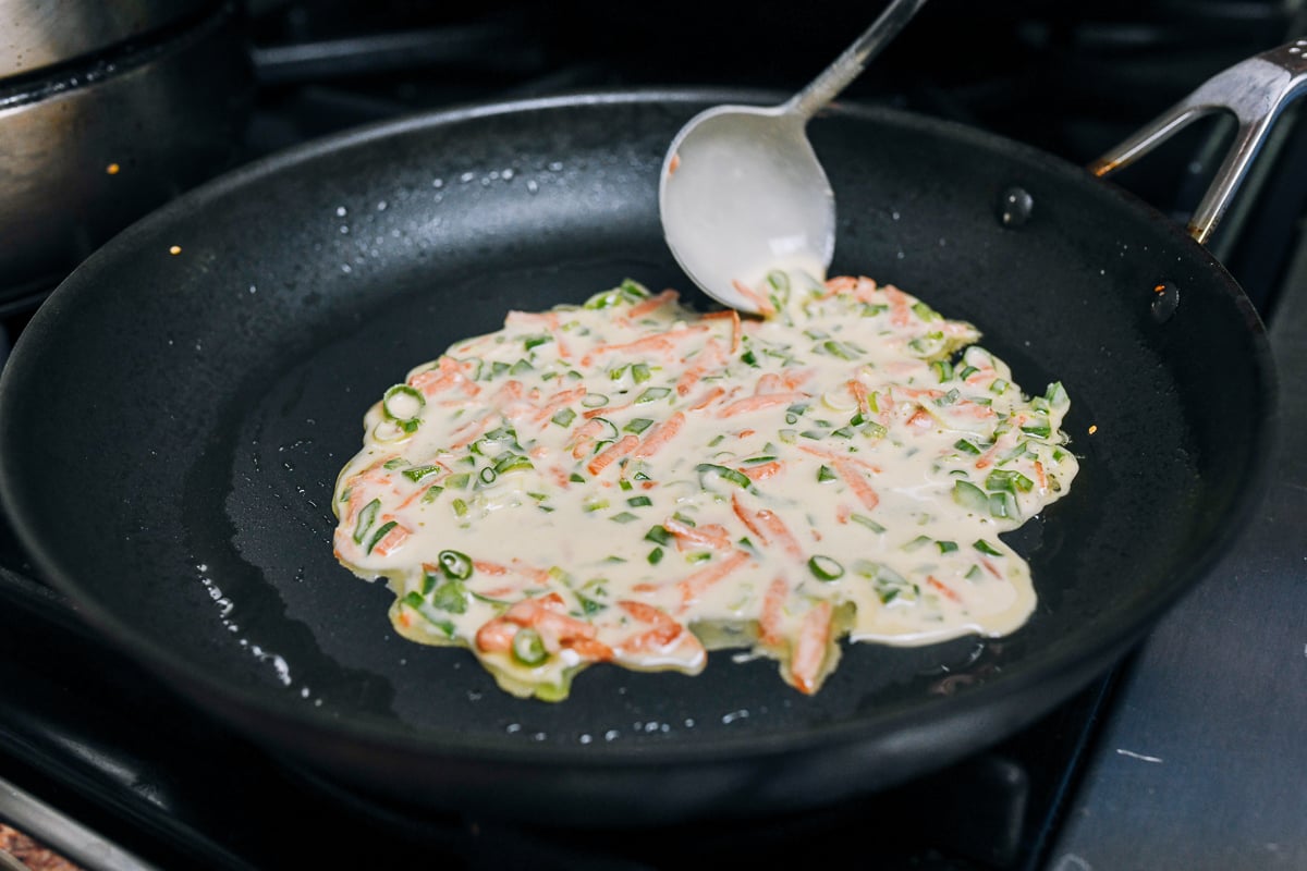 pouring vegetable pancake batter into nonstick pan