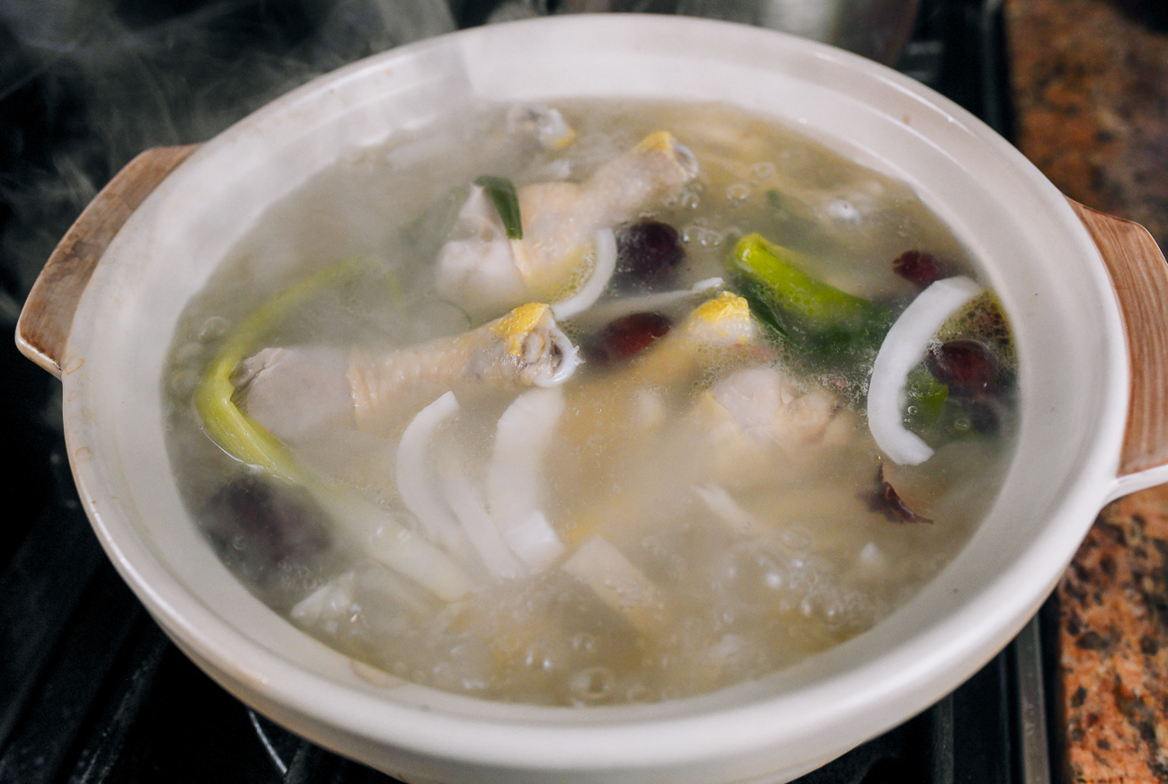 adding chicken legs to soup pot with coconut