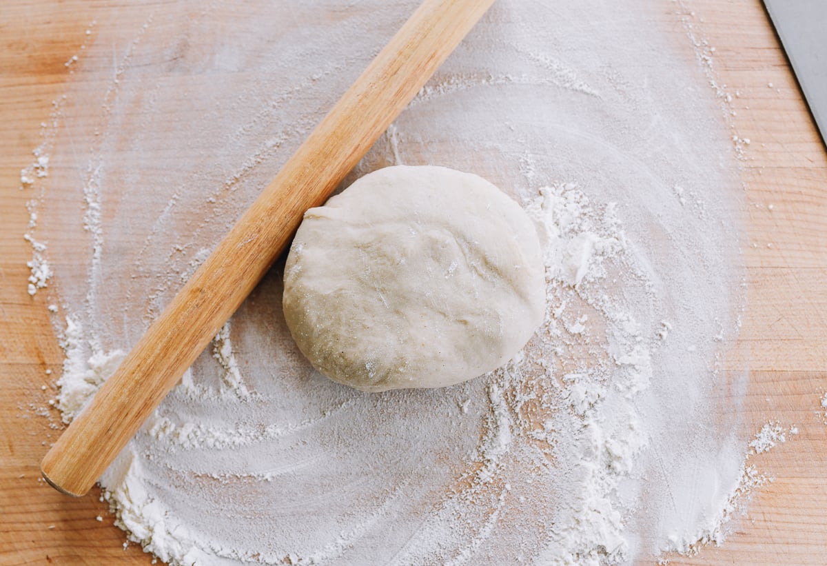 dough ball on floured board with rolling pin