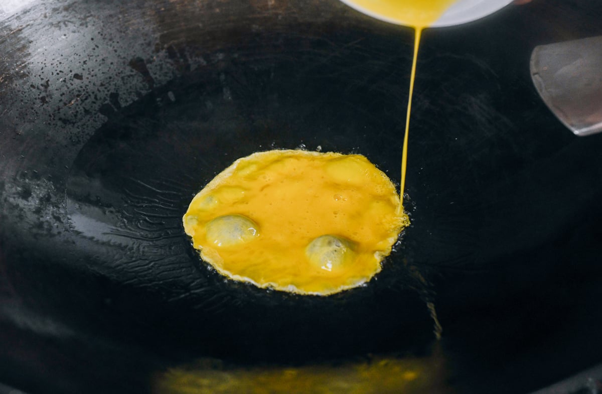 pouring beaten eggs into wok