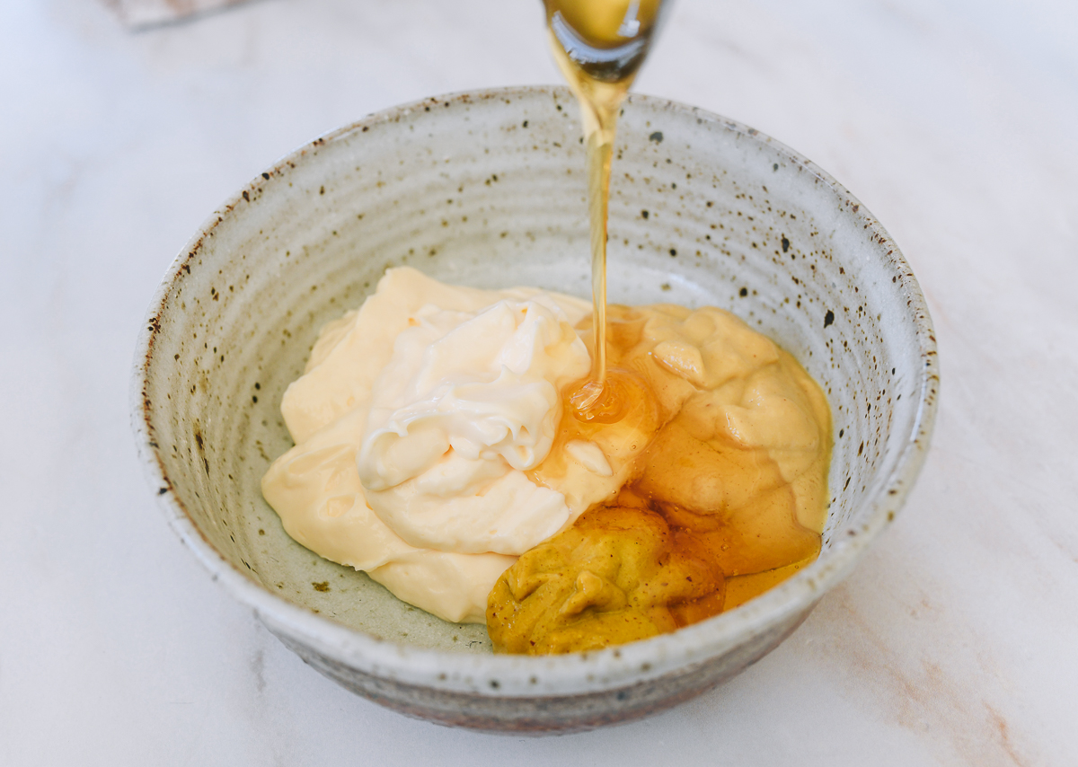 adding honey to honey mustard sauce ingredients in bowl