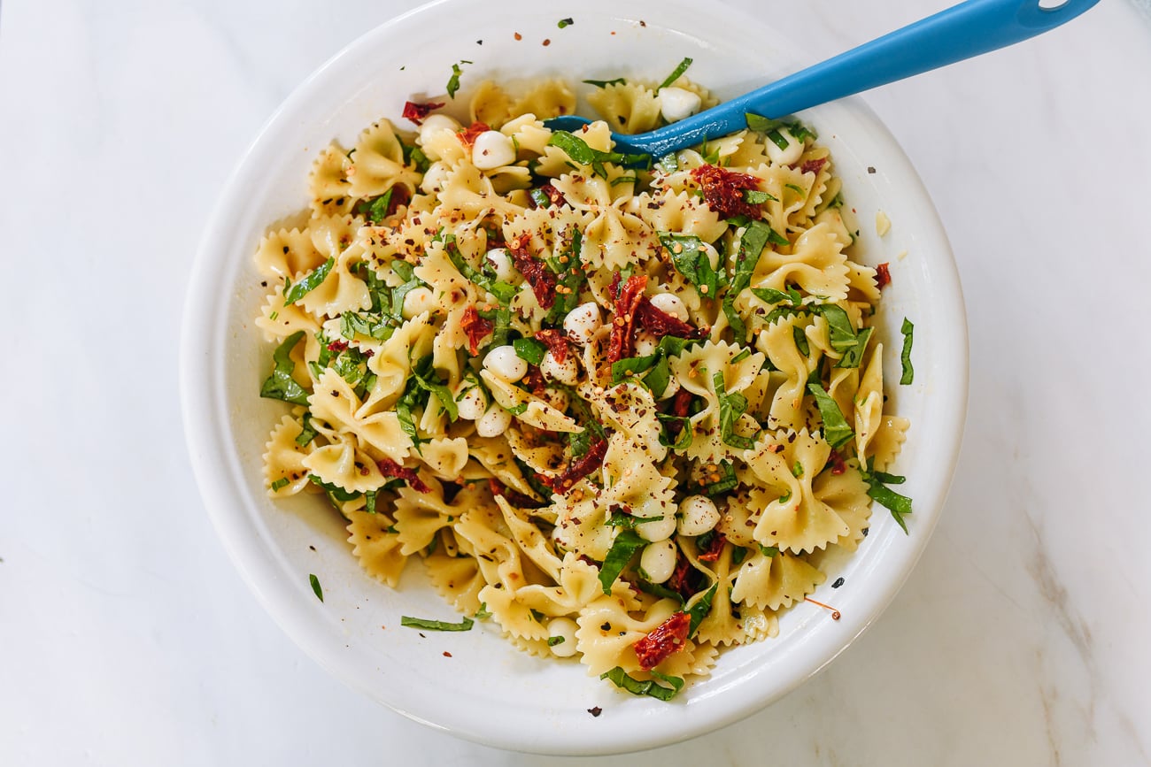 mixing spicy sun-dried tomato pasta salad